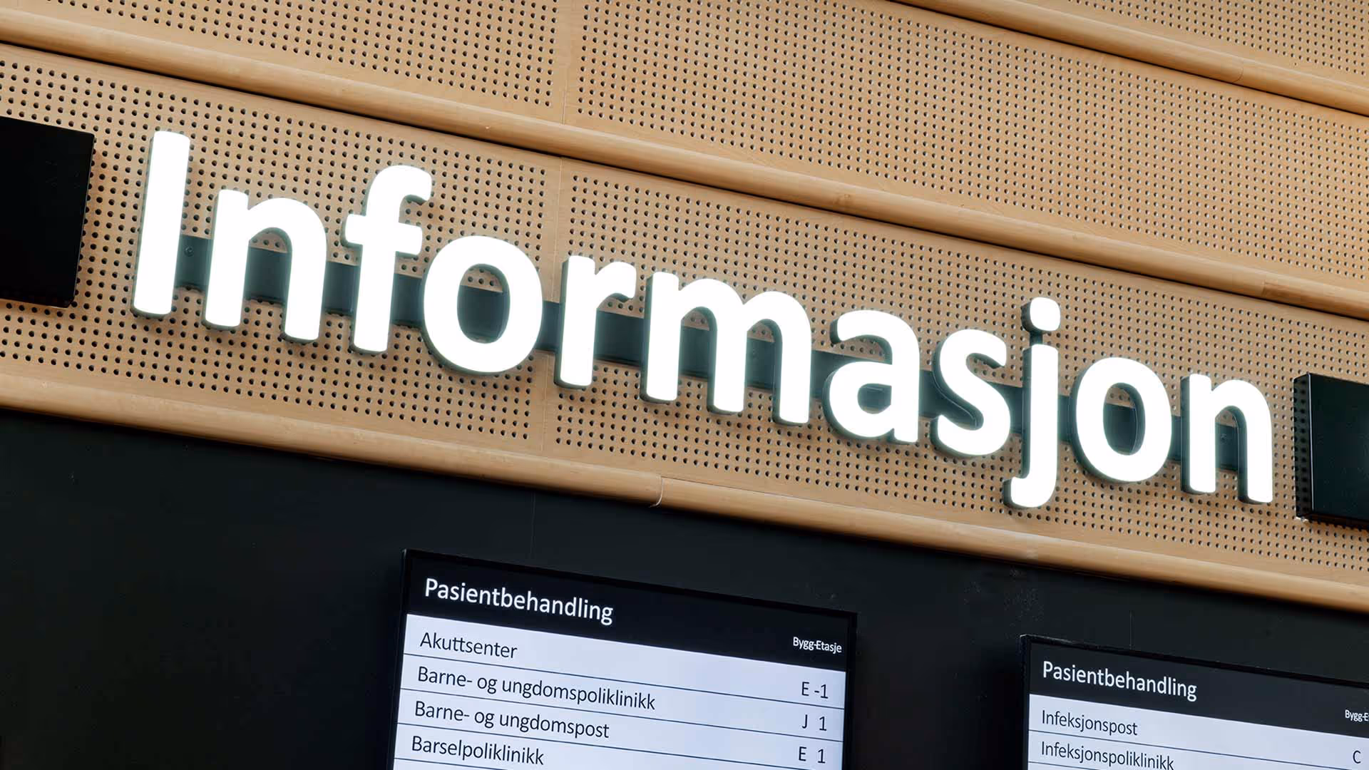 Opplyst skilt med teksten Informasjon over to skjermer som viser pasientbehandling og avdelingsinformasjon på norsk.