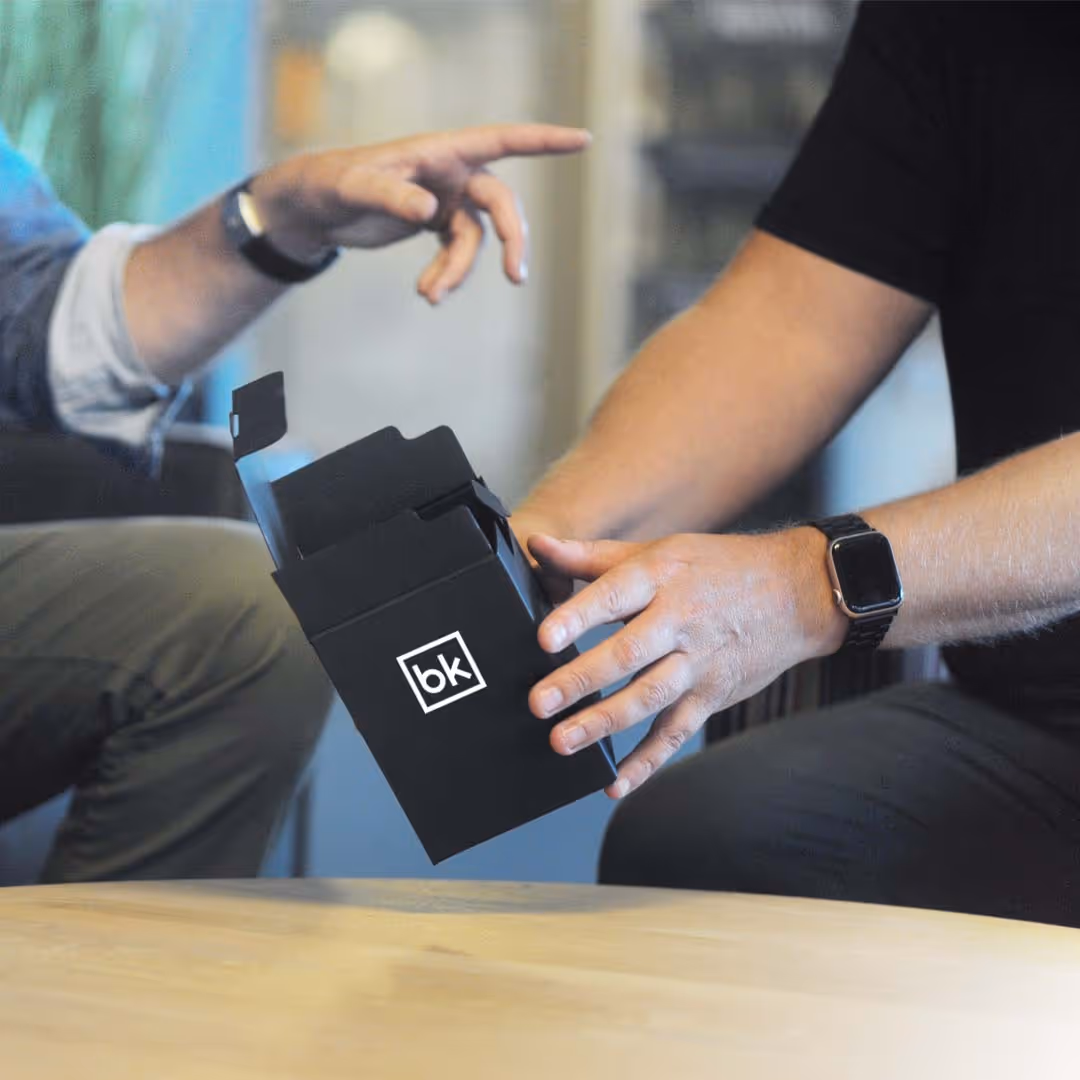 To personer som holder en svart eske med logoen 'bk' over et trebord.