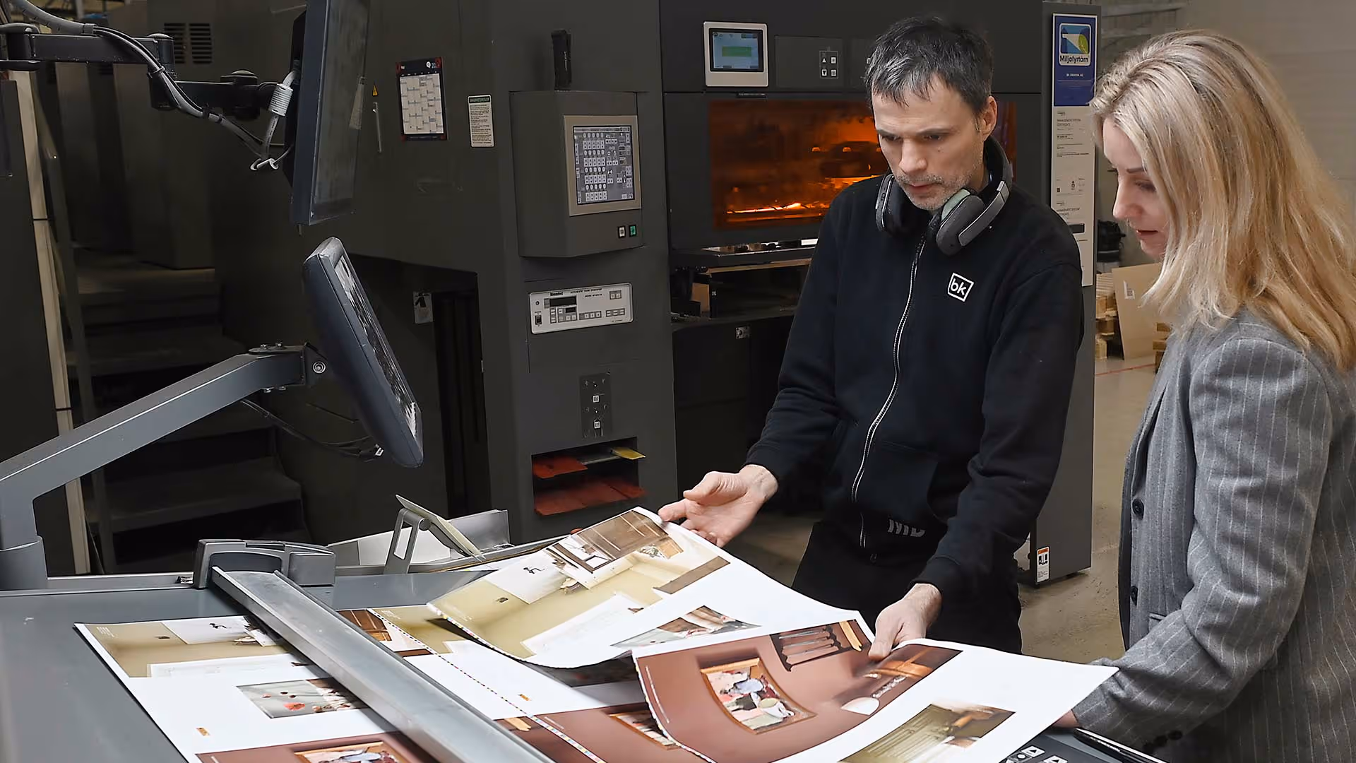 To personer kontrollerer og vurderer trykte ark med bilder på en industriell trykkemaskin.