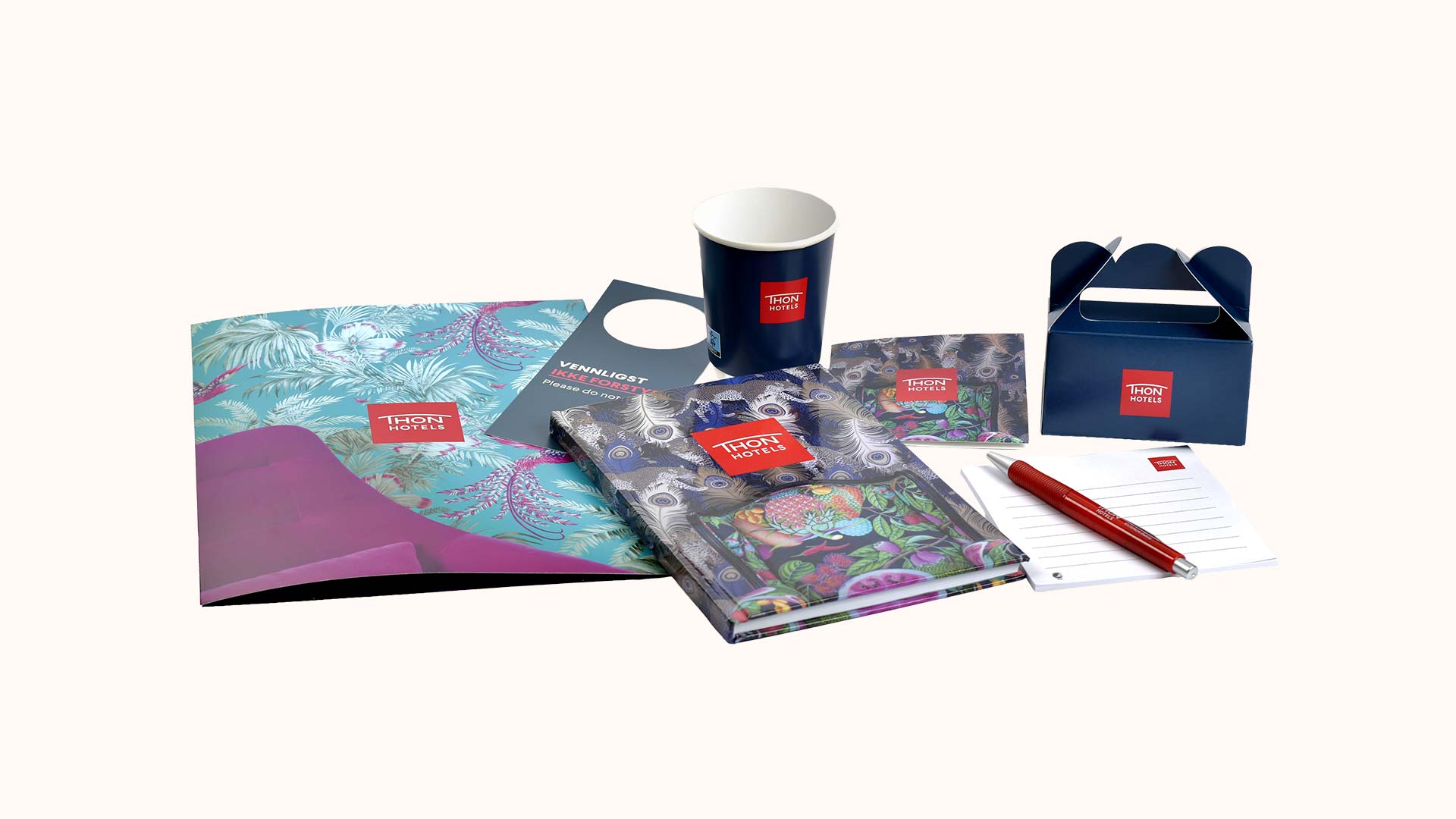 Reise- og kontormateriell med Thon Hotels-logo, inkludert notatbok, penn, kopp, mappe, dørhenger, visittkort og eske med fargerike mønstre.