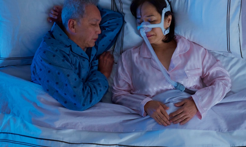 Two older persons sleeping in bad, one with air mask
