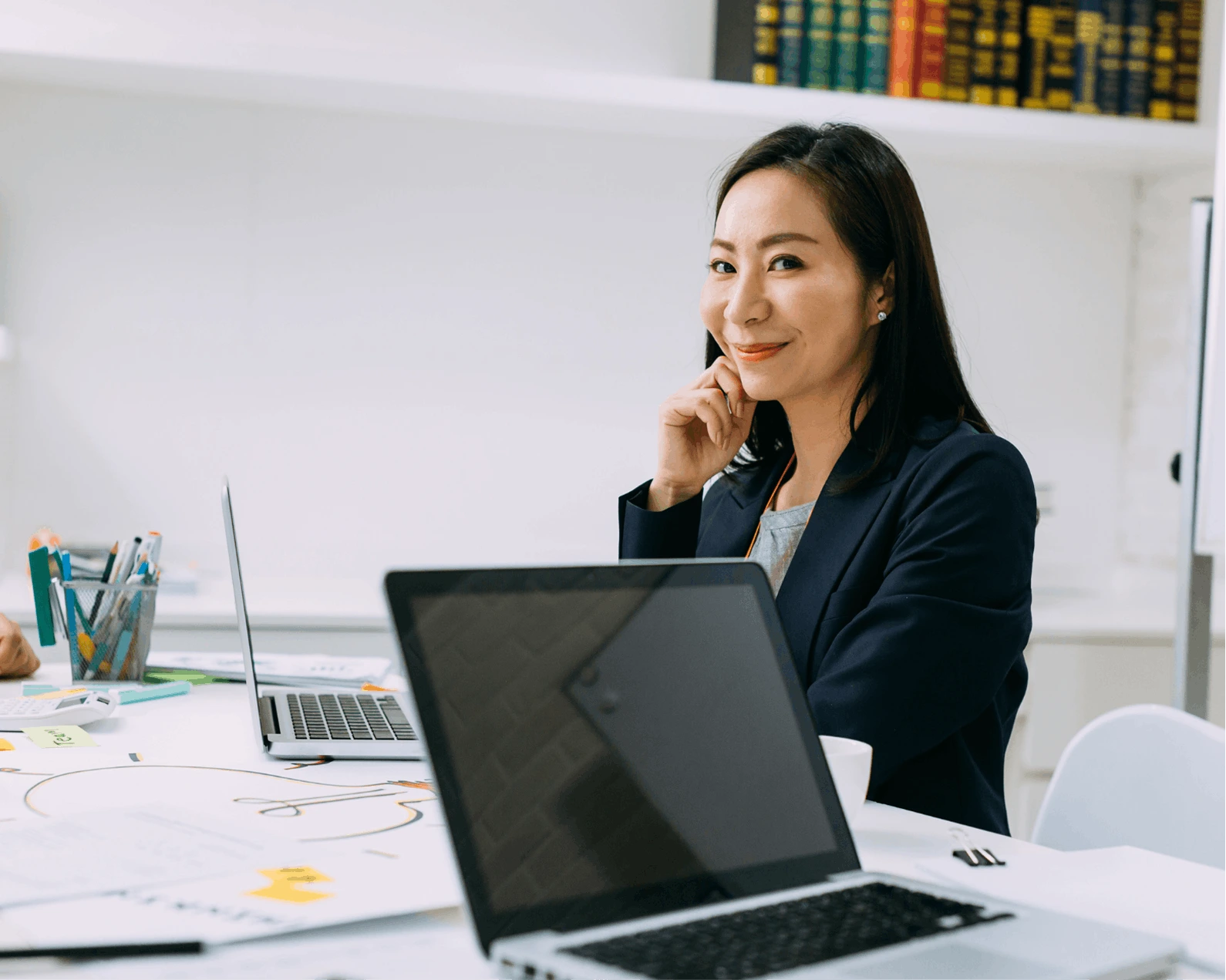 a woman in a navy blue jacket in the office talking on the phone