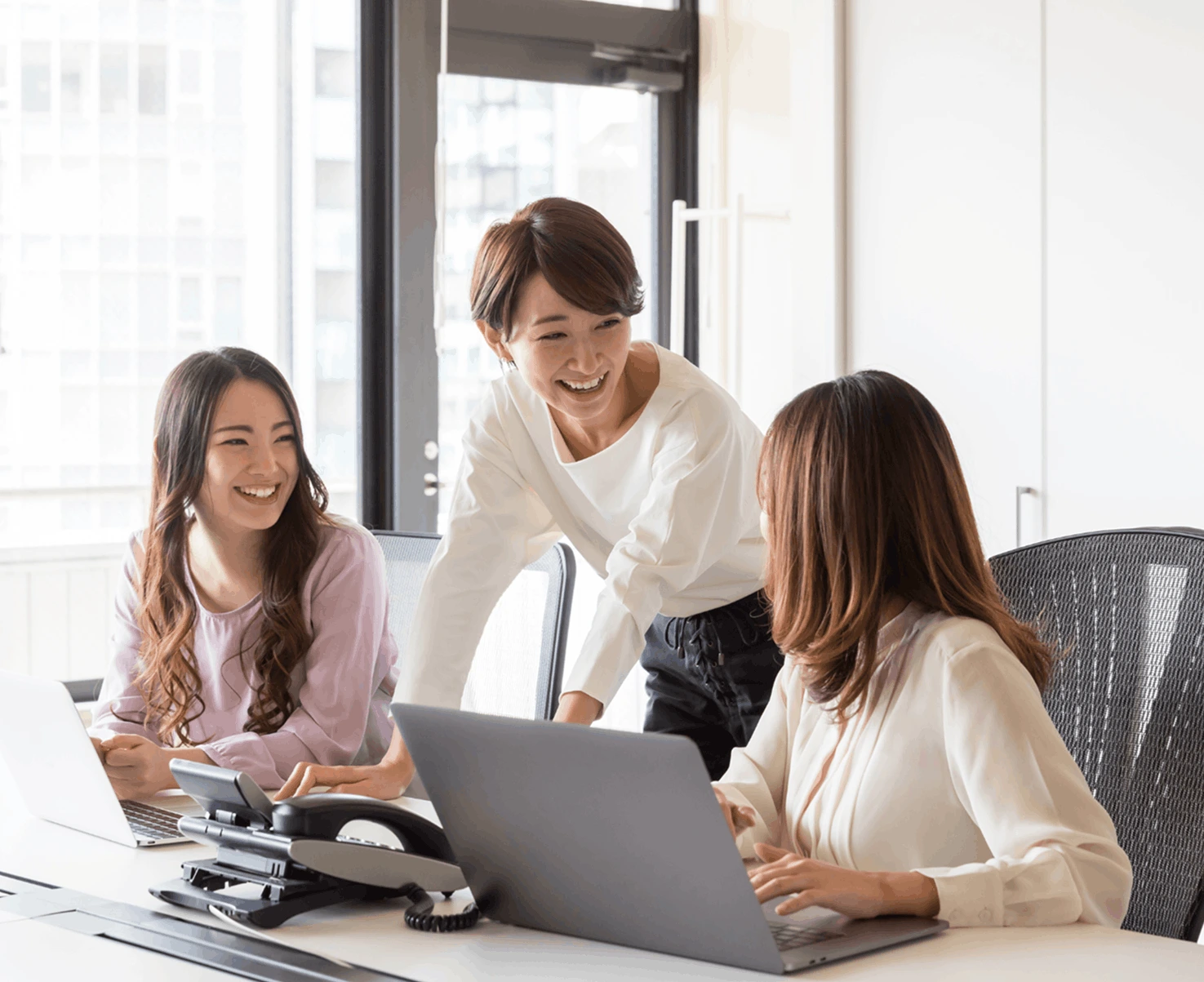 three women in an office at a desk, smiling