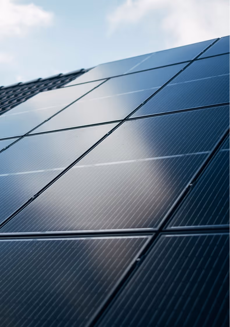 Primo piano di pannelli solari fotovoltaici installati su un tetto, riflettenti il cielo azzurro con alcune nuvole.