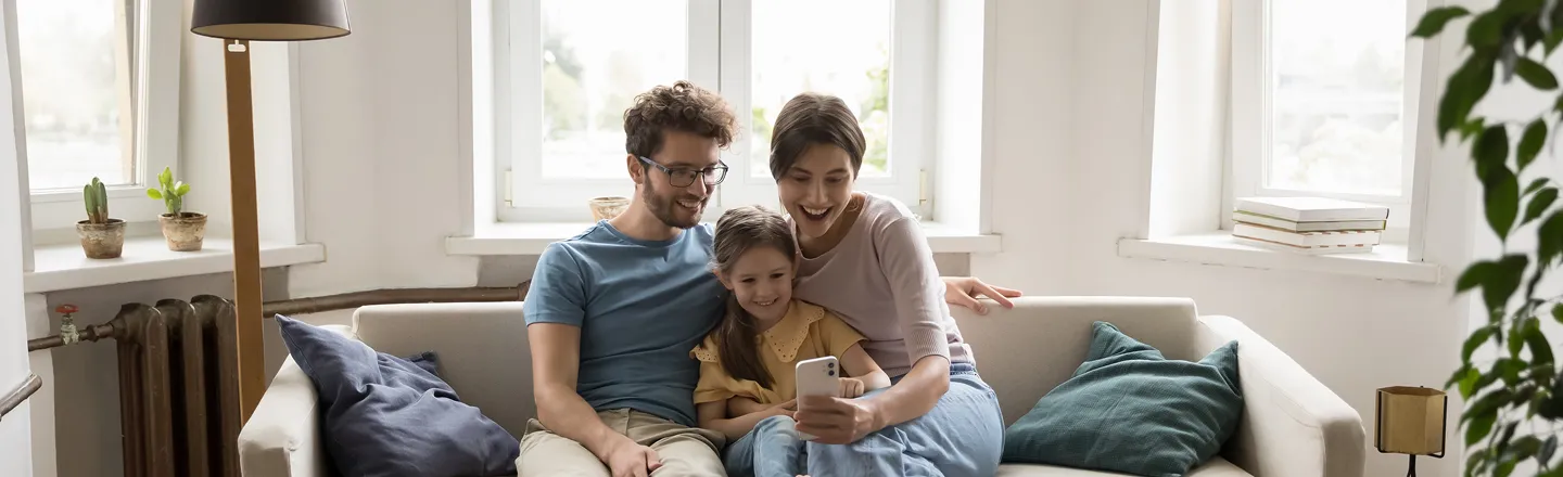 Happy young family sitting on sofa taking a selfie with a smartphone in a bright living room.