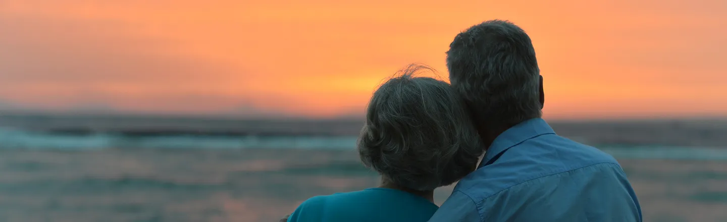 Couple with their backs to the camera watching a sunset over the ocean.