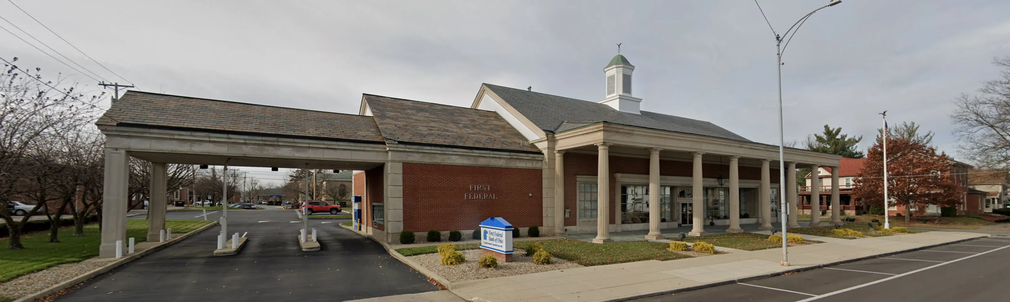 Brick First Federal Bank building with white columns, drive-thru lanes, and a small cupola on the roof.
