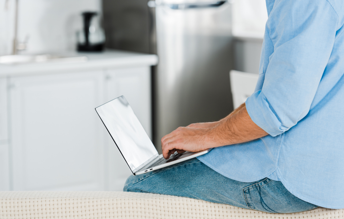 Red barn with stone base surrounded by snow-covered trees and a red fence under a partly cloudy sky.