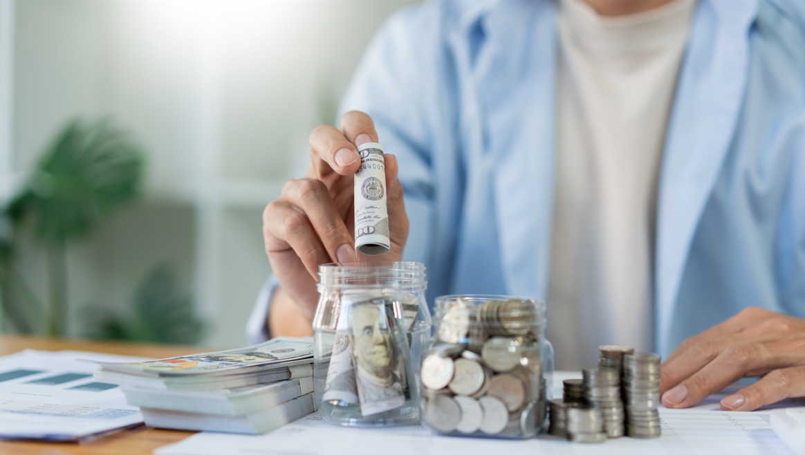 Red barn with stone base surrounded by snow-covered trees and a red fence under a partly cloudy sky.