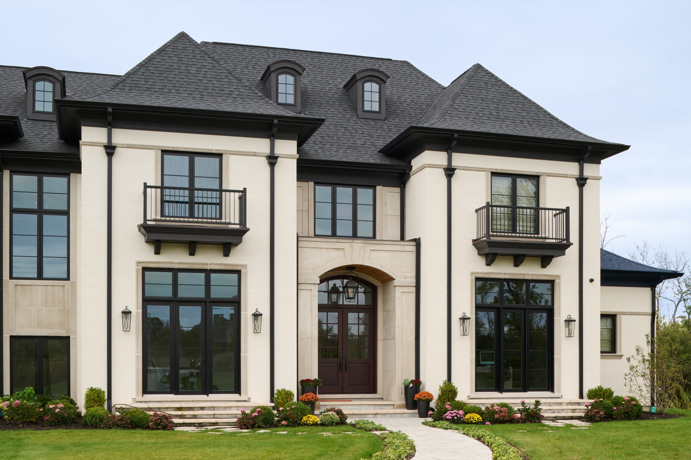 The stately Georgian front facade of the custom Mettawa, IL home by A. Perry Homes, with a cut-limestone entry, Juliet balconies, and a black slate roof.