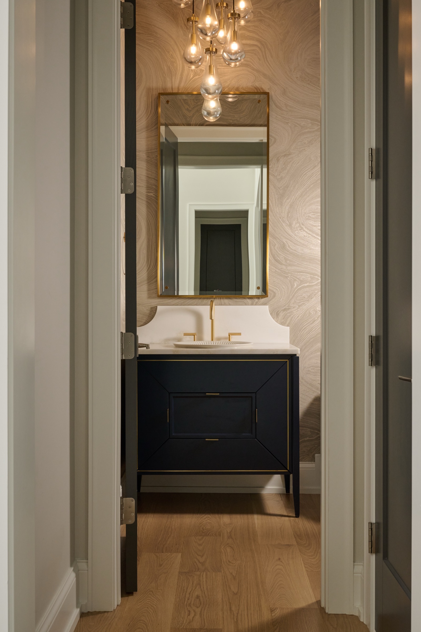 The powder room pairs a navy vanity with brass fixtures, a marbled accent wall, and a brass-framed mirror.