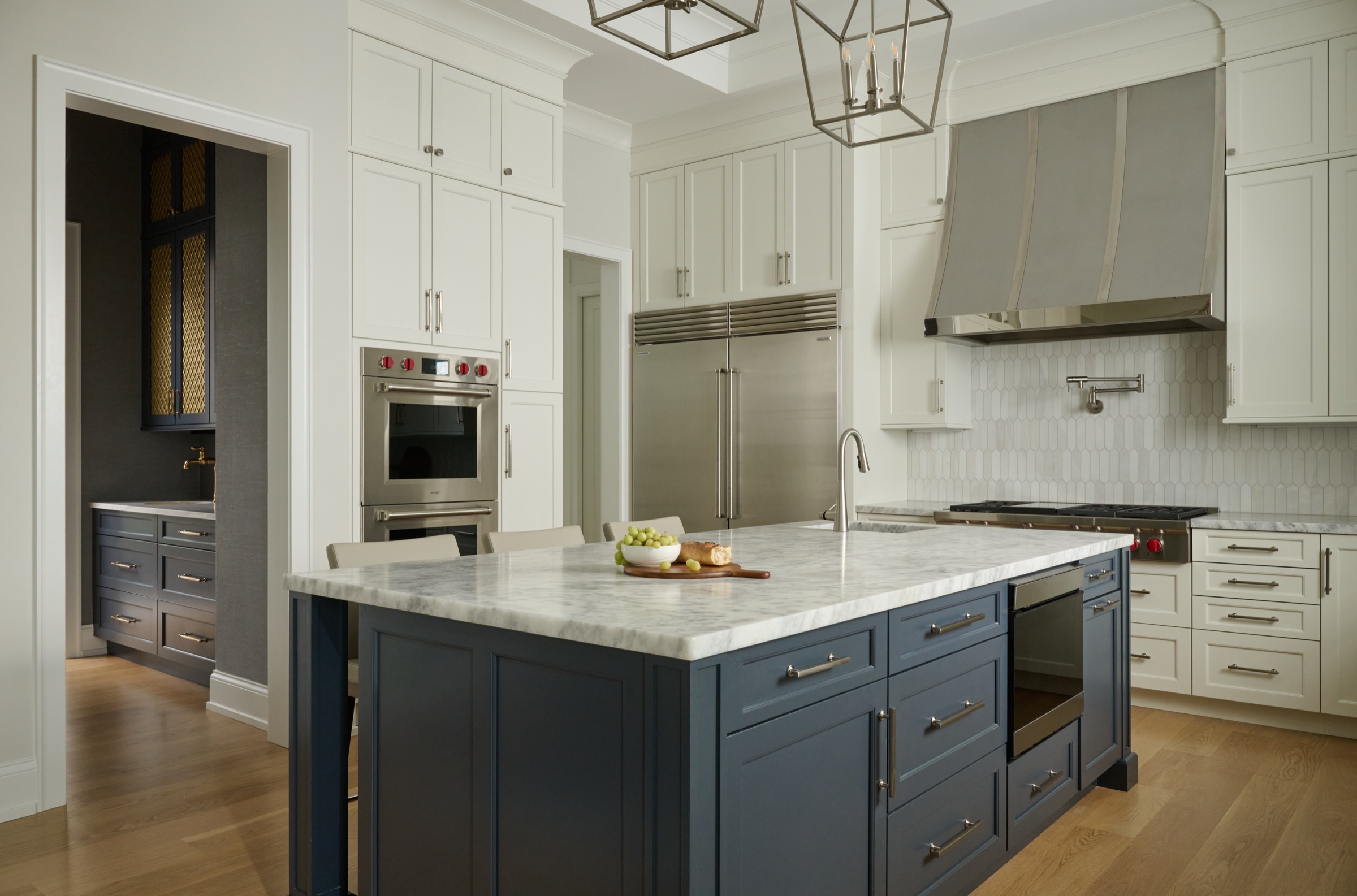 The navy kitchen island topped with marble, paired with professional stainless appliances and a stainless range hood.
