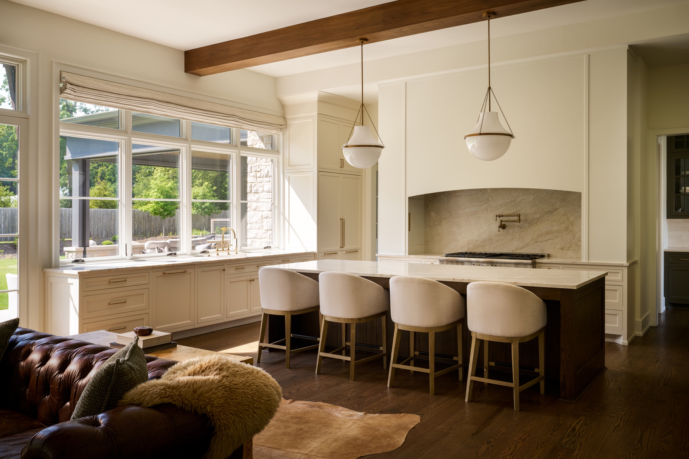 Open-concept kitchen overlooking the beautifully landscaped backyard, with side doors providing direct access to the three-season/sunset porch and outdoor dining area. The kitchen features a grand 10-foot marble island, custom-designed cabinetry, concealed fridge and freezer cabinet doors, and a top-of-the-line La Cornue stove. Transom windows in front of the sink fill the kitchen with natural light and offer views of the landscaped backyard.