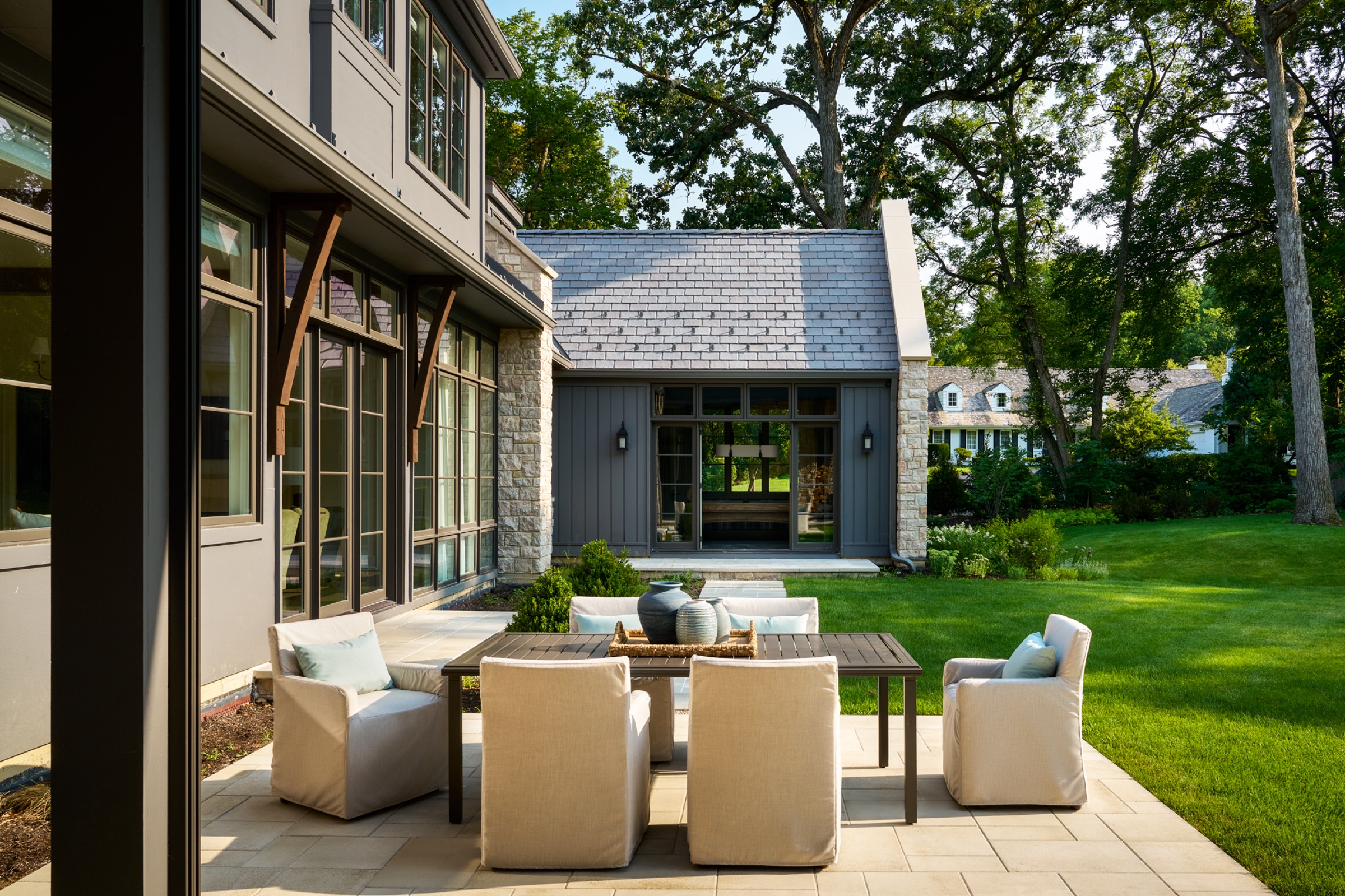 Outdoor dining area adjacent to the three-season room, with direct access to the home's kitchen. A path from the outdoor dining area connects to the billiards room. The home is surrounded by lush landscaping.