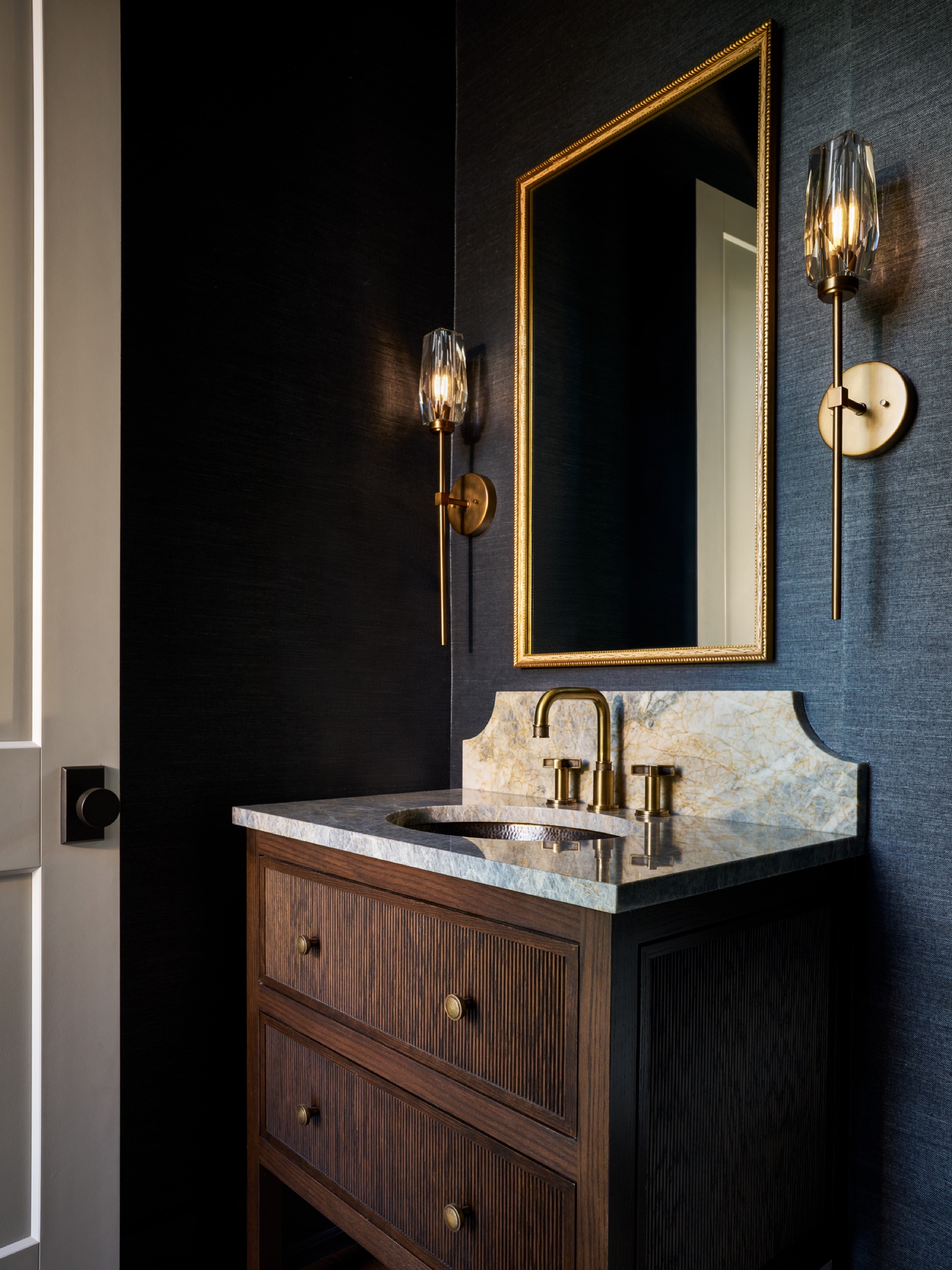 An inspiring and creative powder room filled with an exquisite color palette, gold fixtures, and a moody, textured wallpaper.