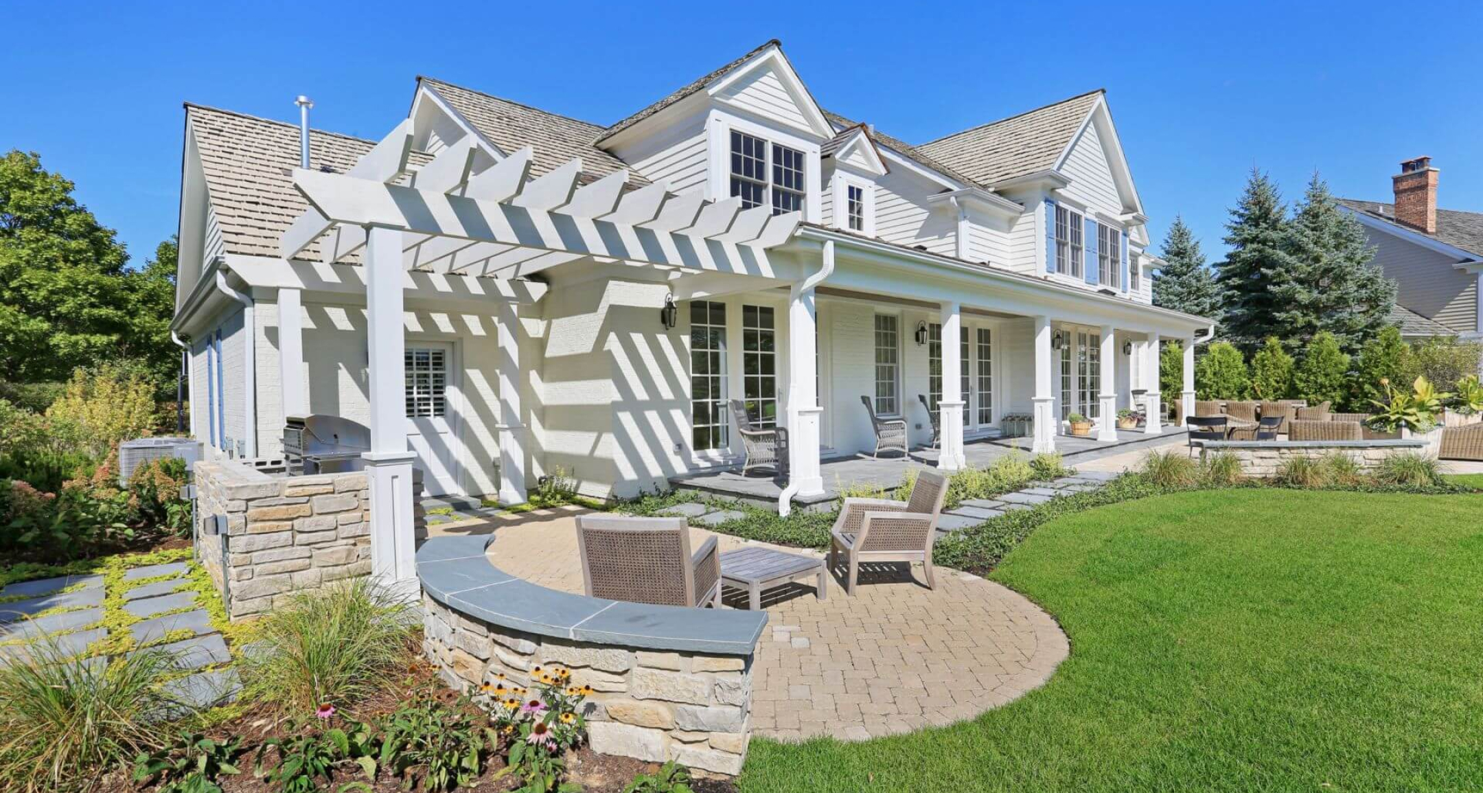 A white traditional custom home in Lake Forest, IL, with a covered back porch and pergola, by A. Perry Homes.