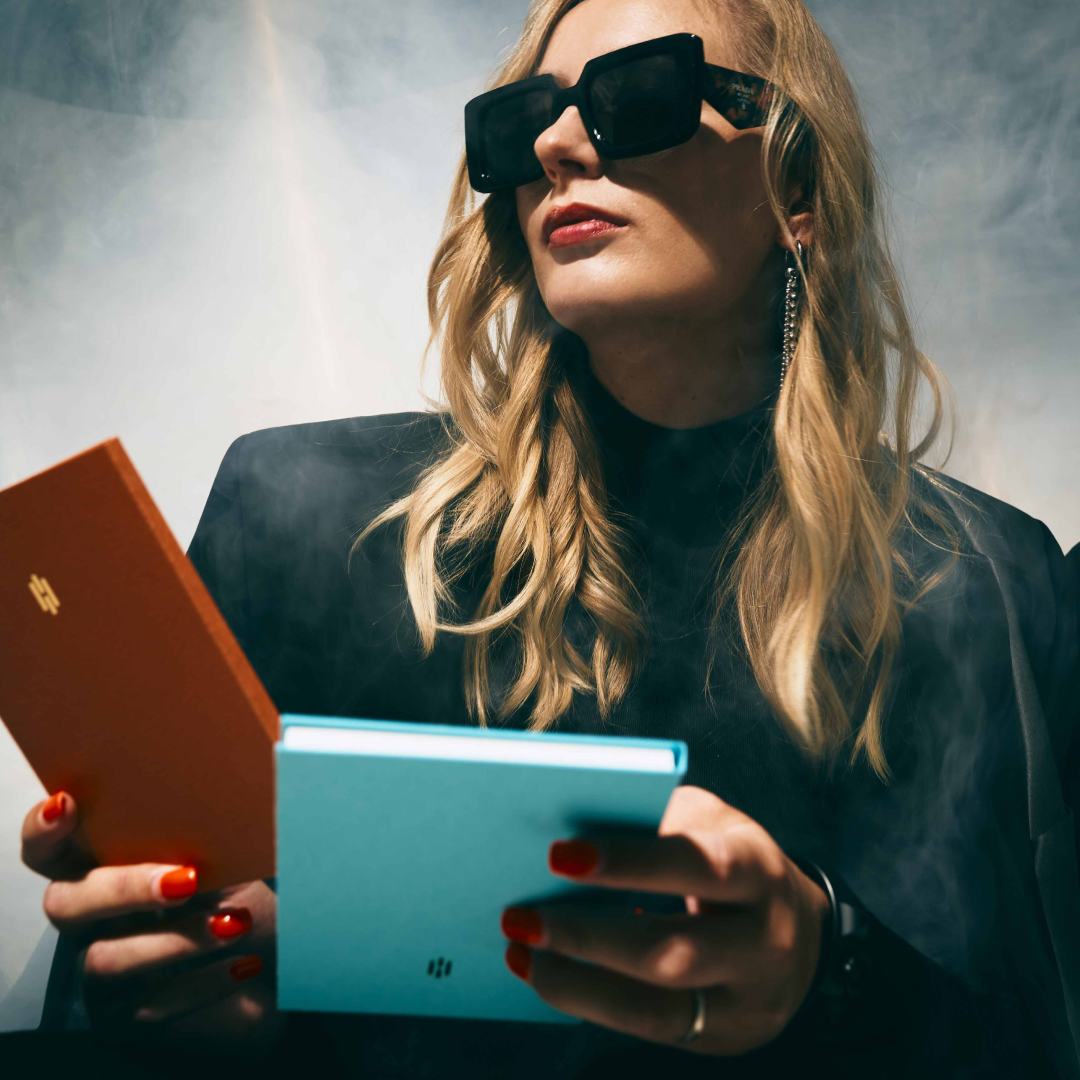 Alexa Vick mit Sonnenbrille hält Bücher in die Kamera.