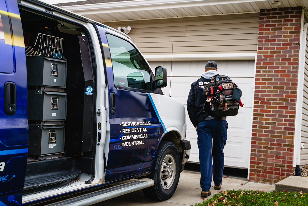 Technician wearing a backpack walking from a service van to a residential garage.