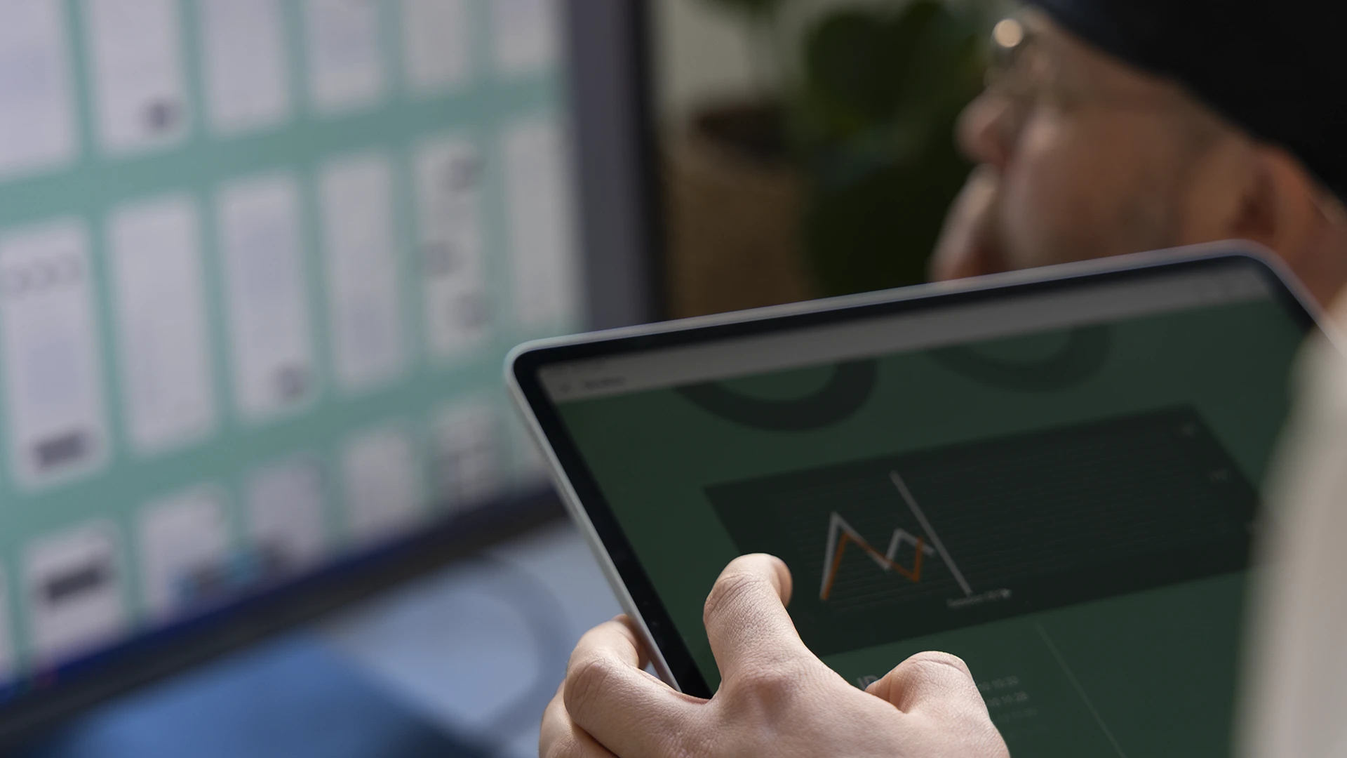 Designer testing UX/UI layouts on an iPad with desktop interface comparison in the background.