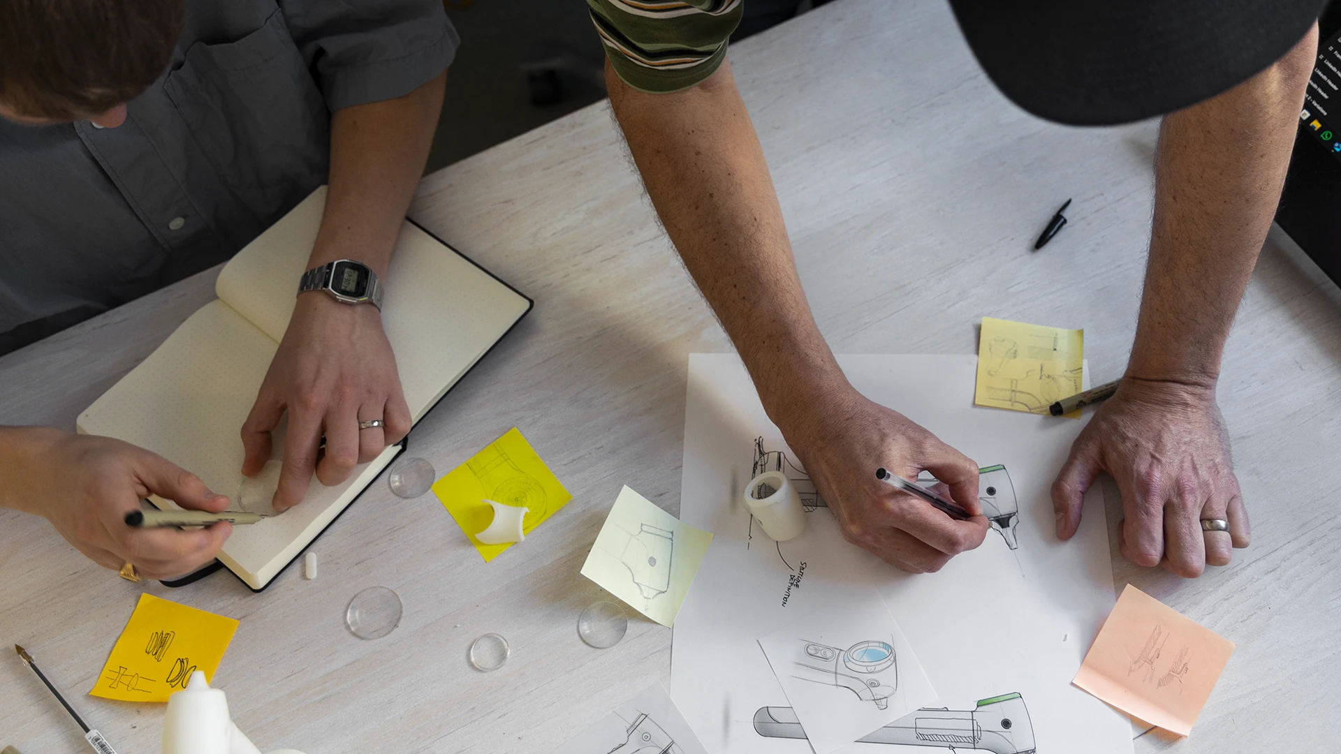 Designers prototyping the OTO K1 otoscope with sketches, lenses and 3D prints during early validation.