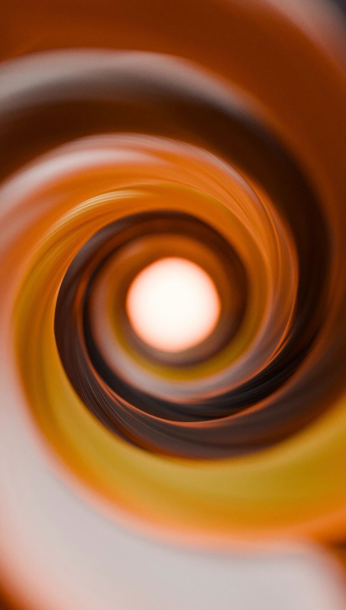 Abstract close-up of a swirling tunnel with warm orange, yellow, and brown tones converging towards a bright center.