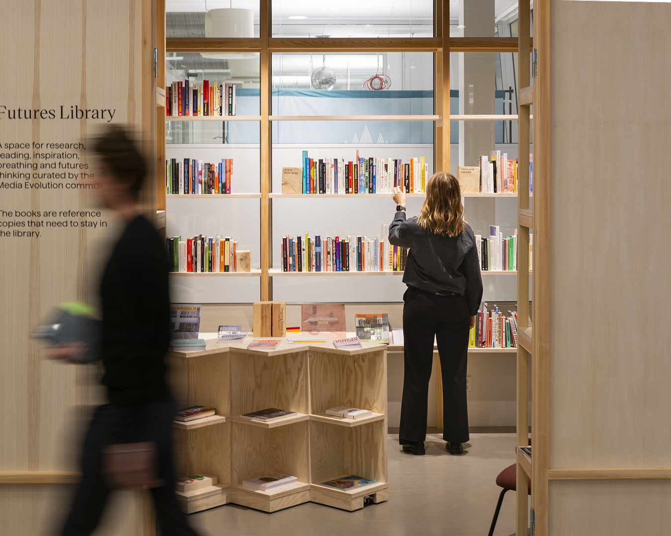 Person browsing books in a modern library with wooden shelves and a hexagonal wooden display table.