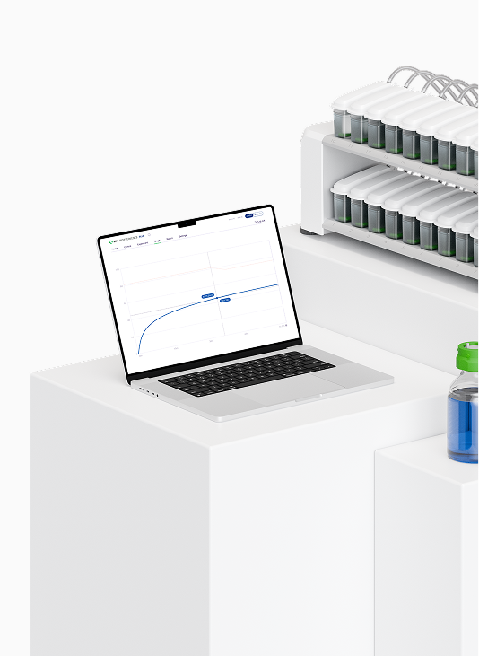 Laptop showing a scientific graph next to a device holding multiple small containers with green lids.