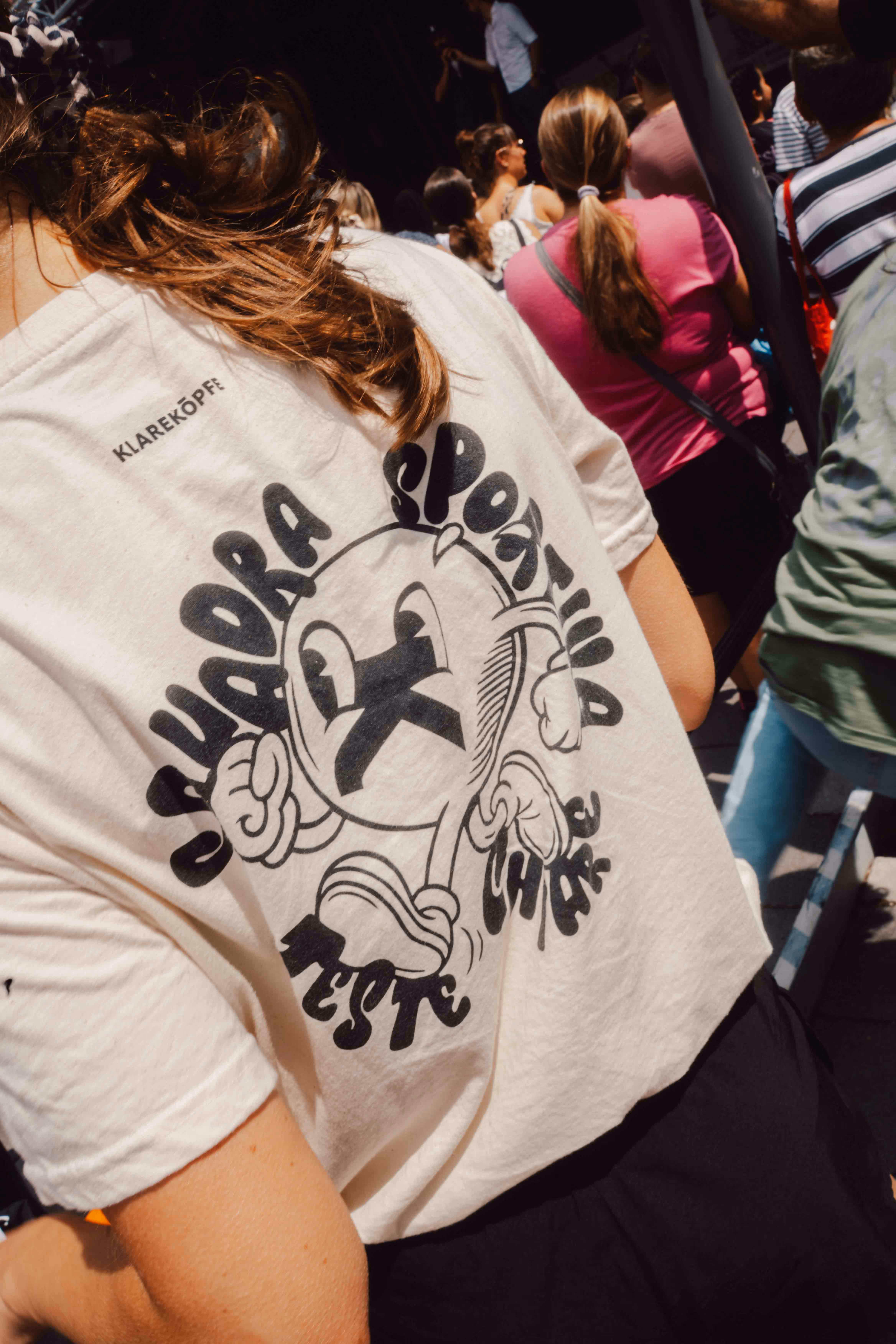 Person trägt weißes T-Shirt mit Aufdruck „Squadra sportiva teste chiare" und Cartoon-Figur.