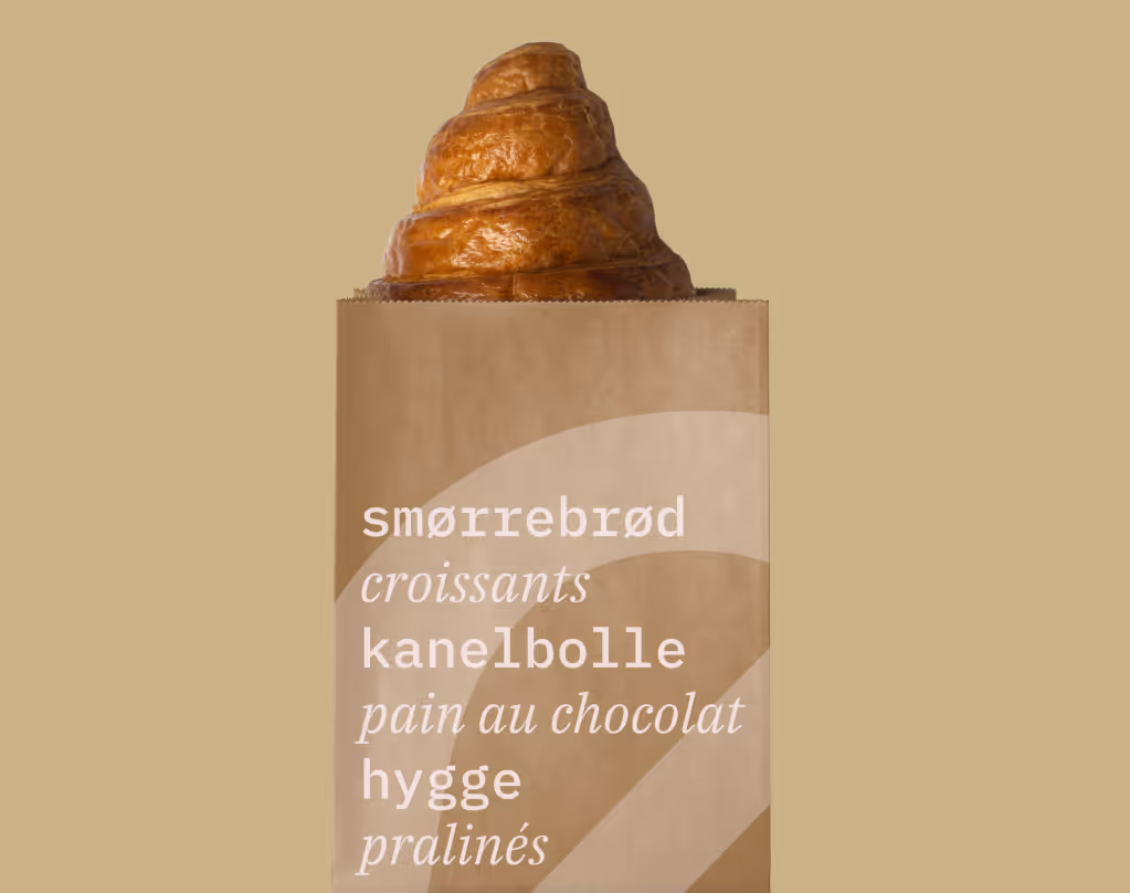 Braunes Croissant ragt aus einer braunen Papiertüte mit Text in verschiedenen Sprachen heraus.