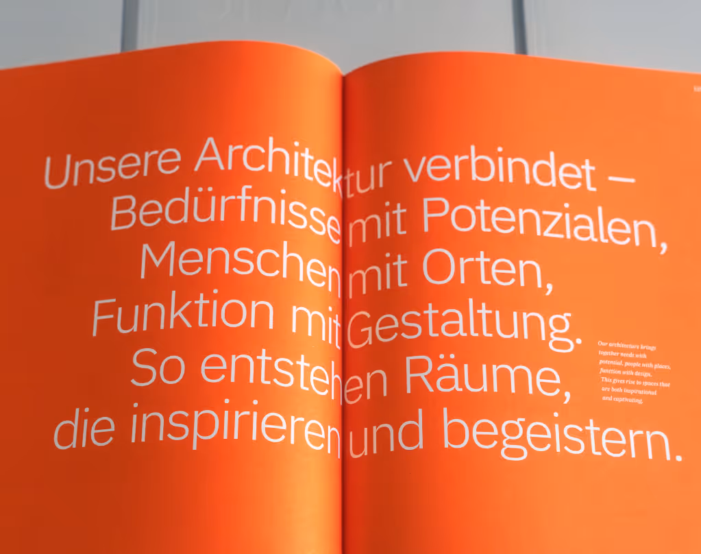 Offenes Imagebook mit Text in Weiß auf orangefarbene Seiten über Architektur, Räume und Inspiration.
