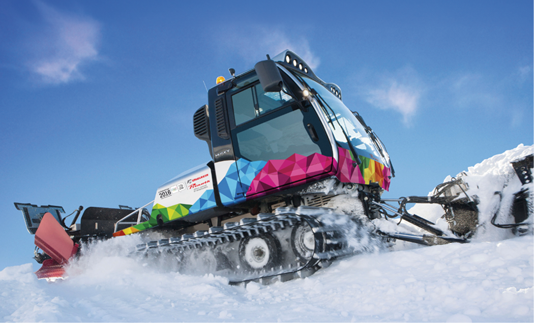 Snow groomer machine with colorful geometric patterns clearing snow under blue sky.