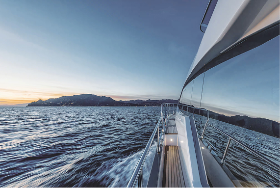 View from a yacht's side deck showing water, mountains, and a sunset sky.