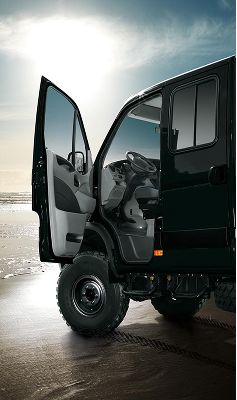 Open door of black off-road vehicle showing steering wheel and dashboard on a sandy beach.