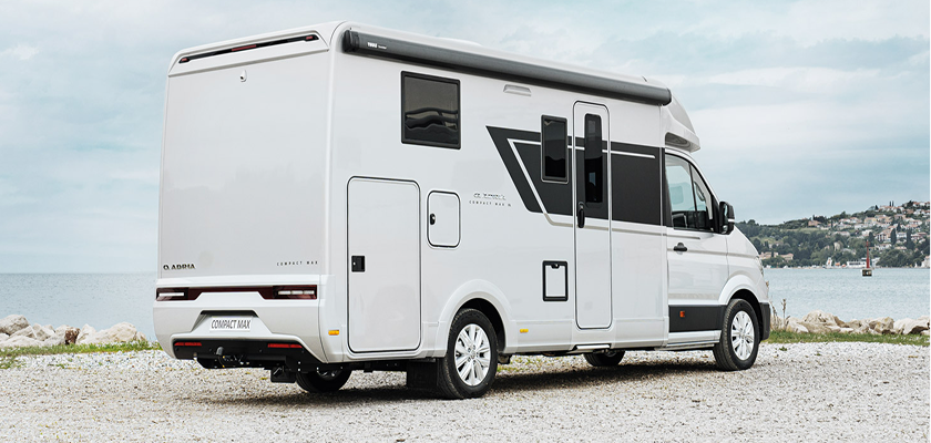 White Adria Compact Max camper van parked on gravel with a lake and hills in the background.