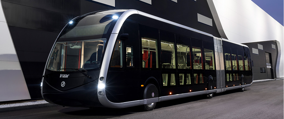 Modern black articulated bus with large windows parked near a building with geometric design.