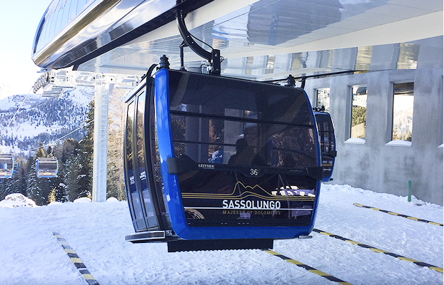 Blue gondola cabin labeled Sassolungo Majestic Dolomites at a snowy mountain ski lift station.