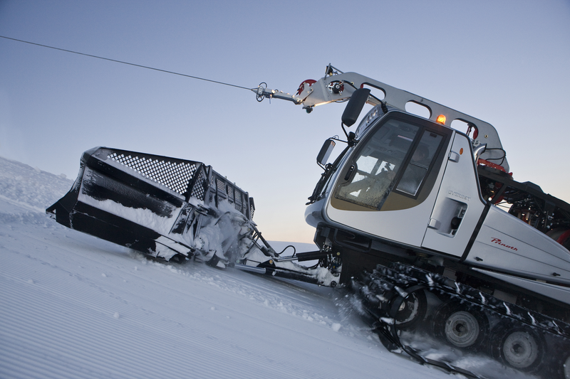 Snow grooming machine smoothing snow on a slope during early morning or evening light.