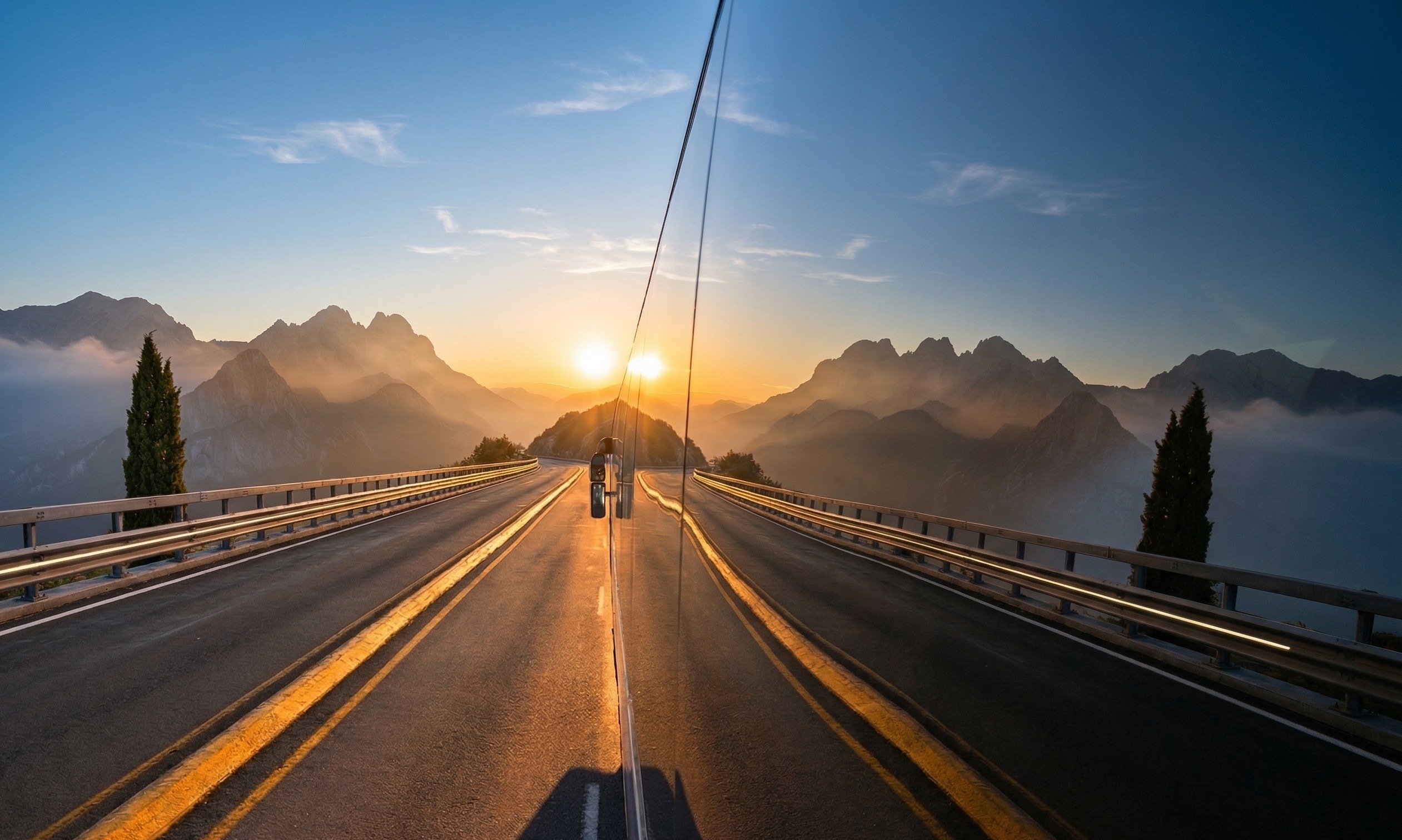 Sunset over a mountain road reflected on the side of a vehicle driving on the highway.