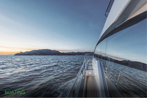 Side view of a boat moving on water near mountains at sunset with a clear blue sky.
