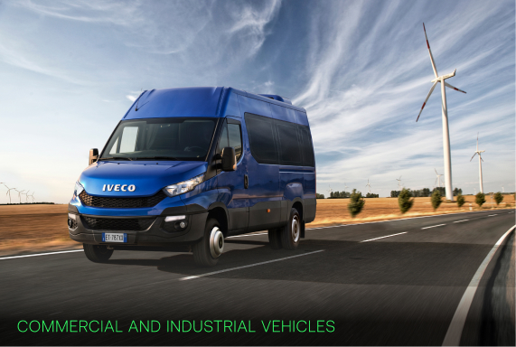 Blue Iveco commercial van driving on road with wind turbines and fields in background under a cloudy sky.
