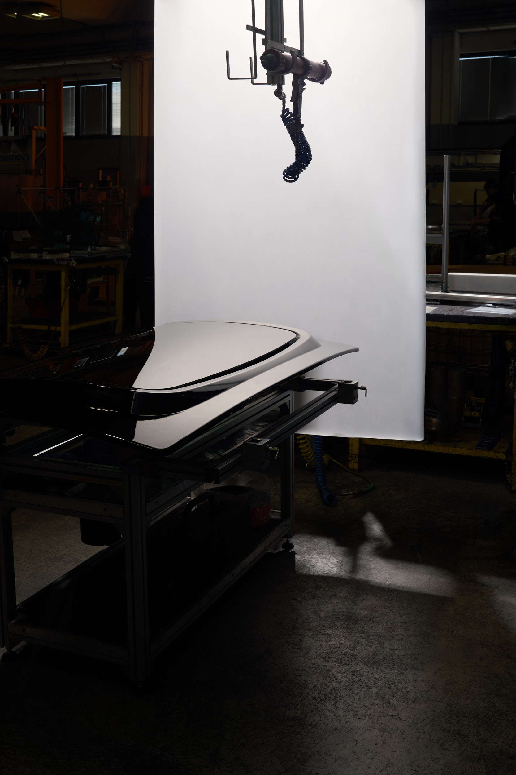 Glossy black car roof panel on a metal table in a dimly lit industrial workshop.