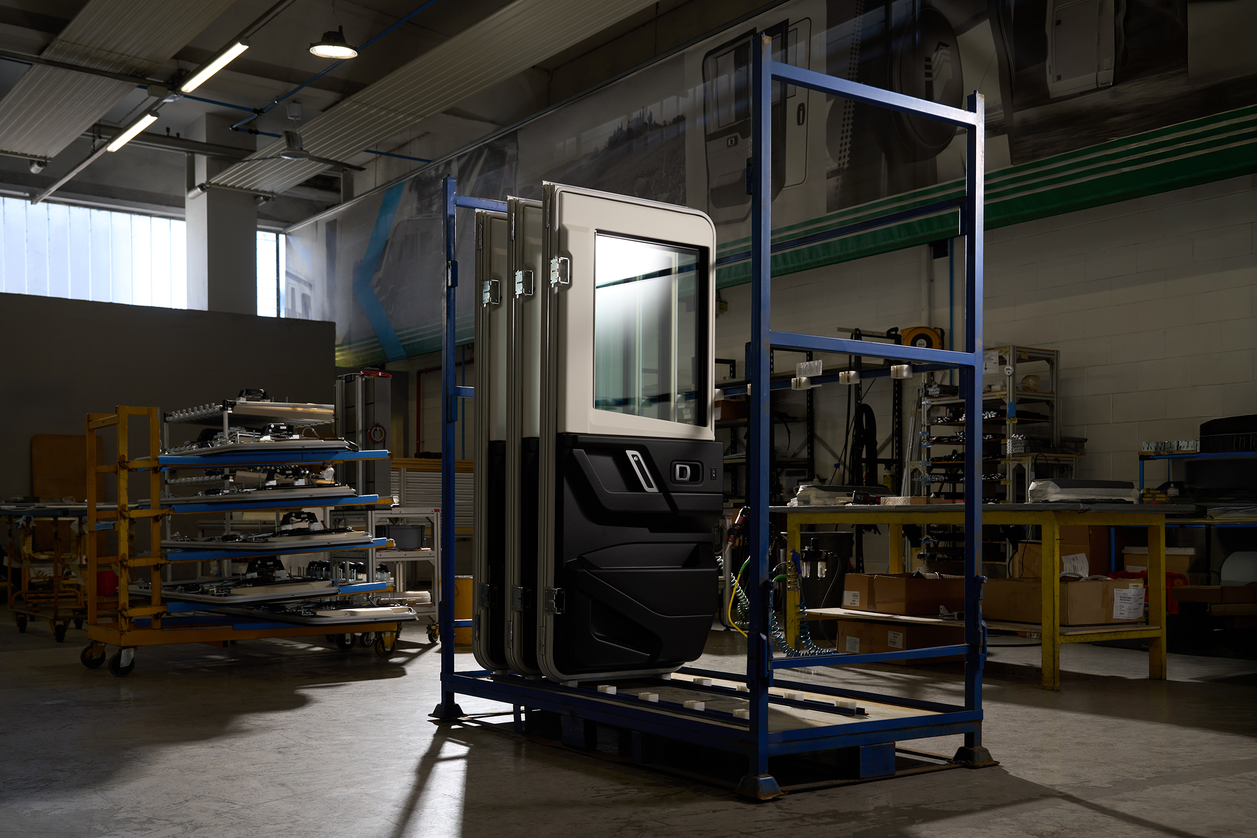 Vehicle door panels stored upright on a blue metal rack inside a dimly lit industrial workshop.