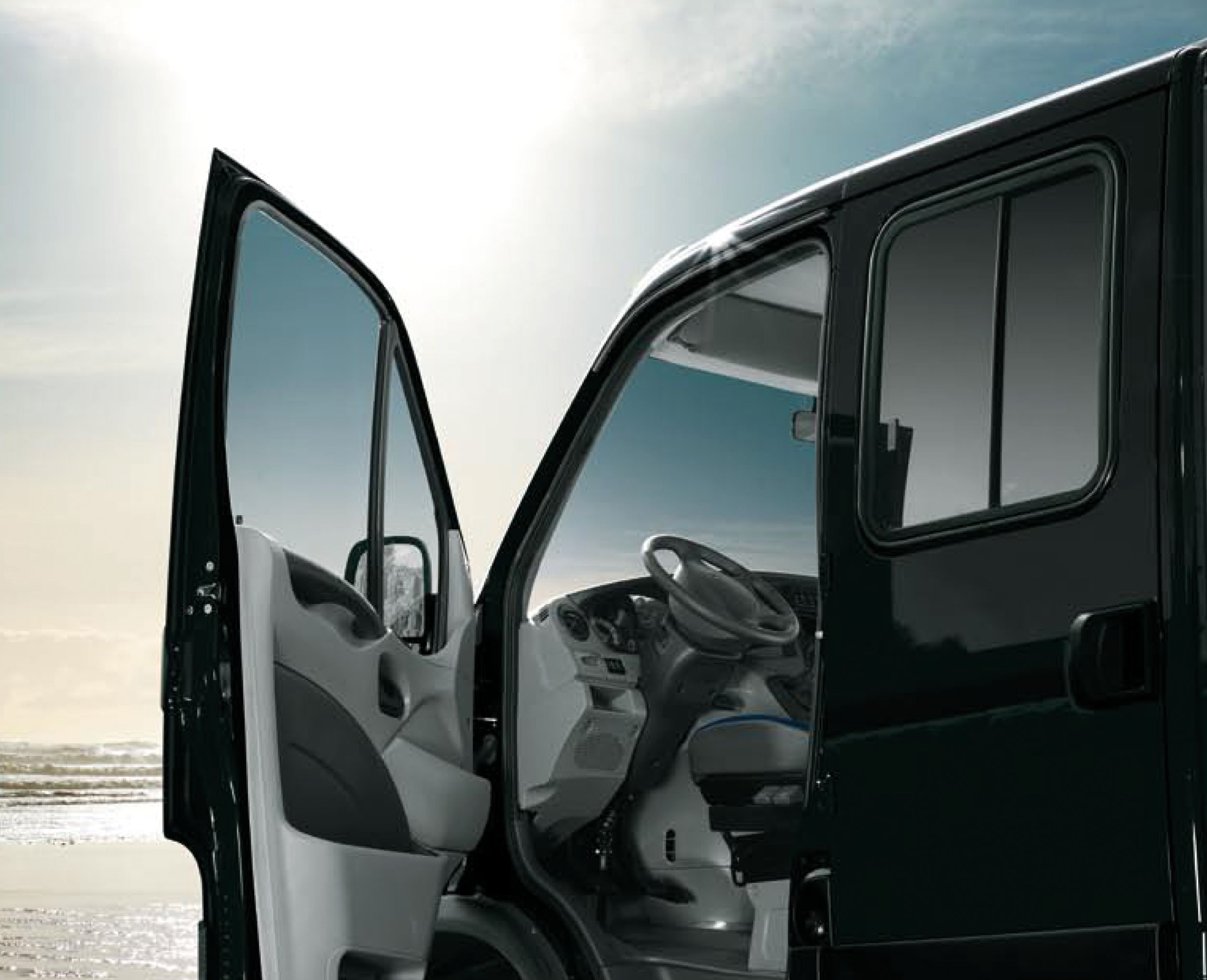 Open driver's side door showing steering wheel and interior of a black vehicle at sunrise or sunset.