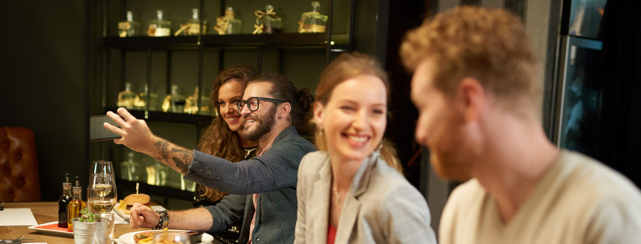 Couples enjoying at a dinner while a couple takes a selfie in the background