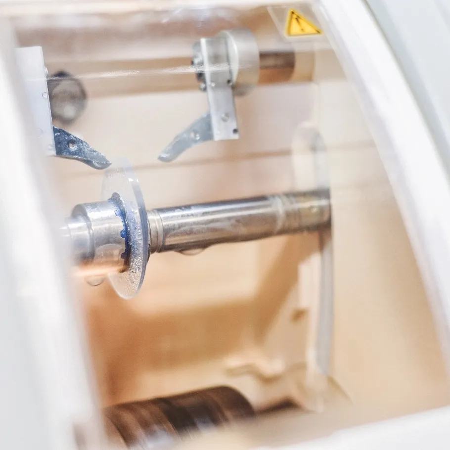 Nahaufnahme einer Metallwelle und mechanischer Teile in einer Schutzabdeckung eines Geräts zum schleifen von Brillengläsern.