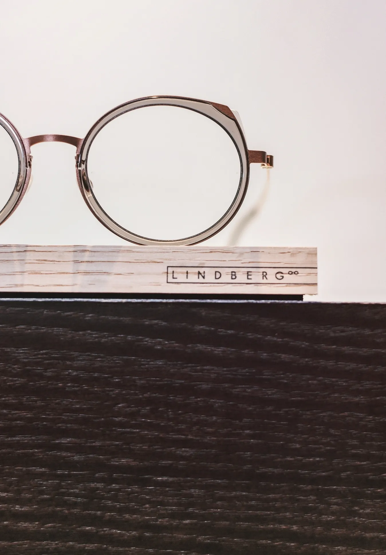 Brille mit rundem Rahmen aus Metall auf einem Holzständer mit der Aufschrift ‚LINDBERG‘.