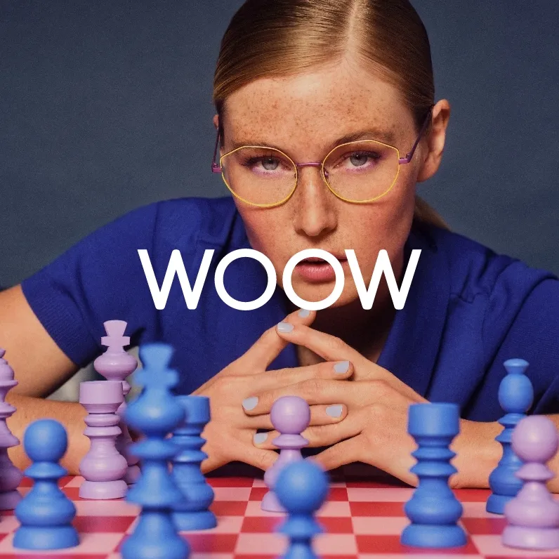 Markenbild WOOW. Frau mit glatten, zurückgebundenen Haaren und runden gelb-lila Brillen blickt konzentriert über ein Schachbrett mit blauen und lila Figuren.