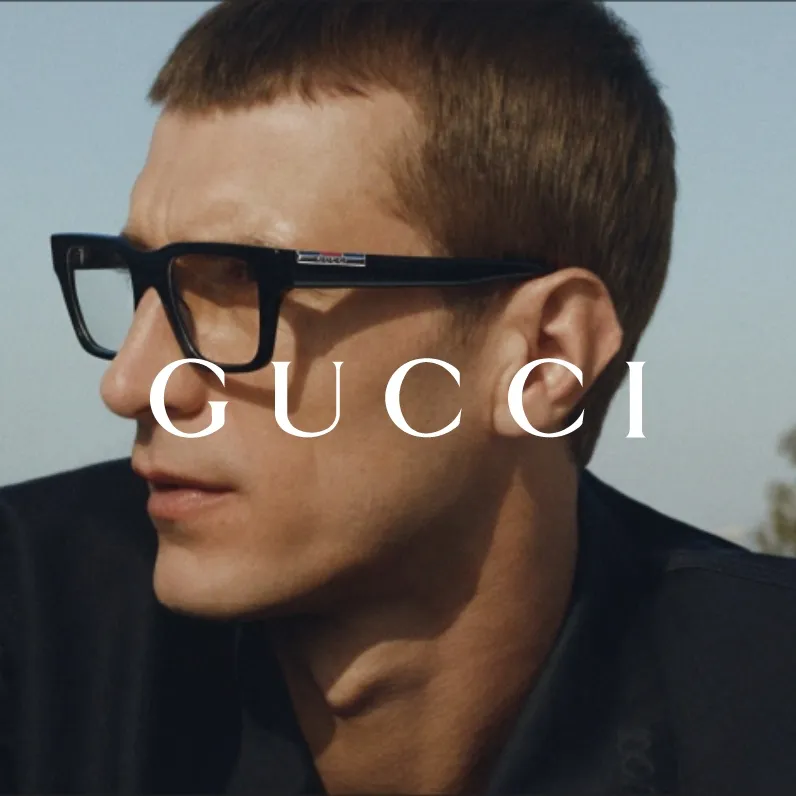 Markenbild GUCCI. Porträt eines Mannes mit kurzen braunen Haaren und schwarzen Gucci-Brillen vor hellem Himmel.