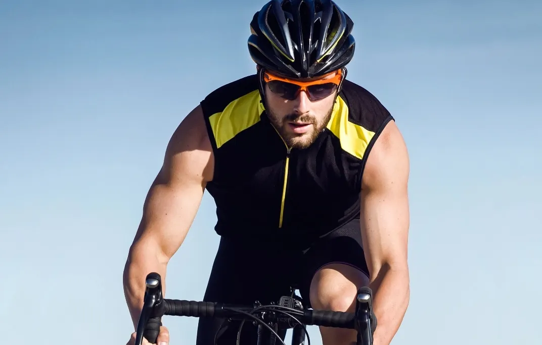 Mann mit Fahrradhelm und Sonnenbrille fährt auf einem Rennrad bei klarem Himmel.