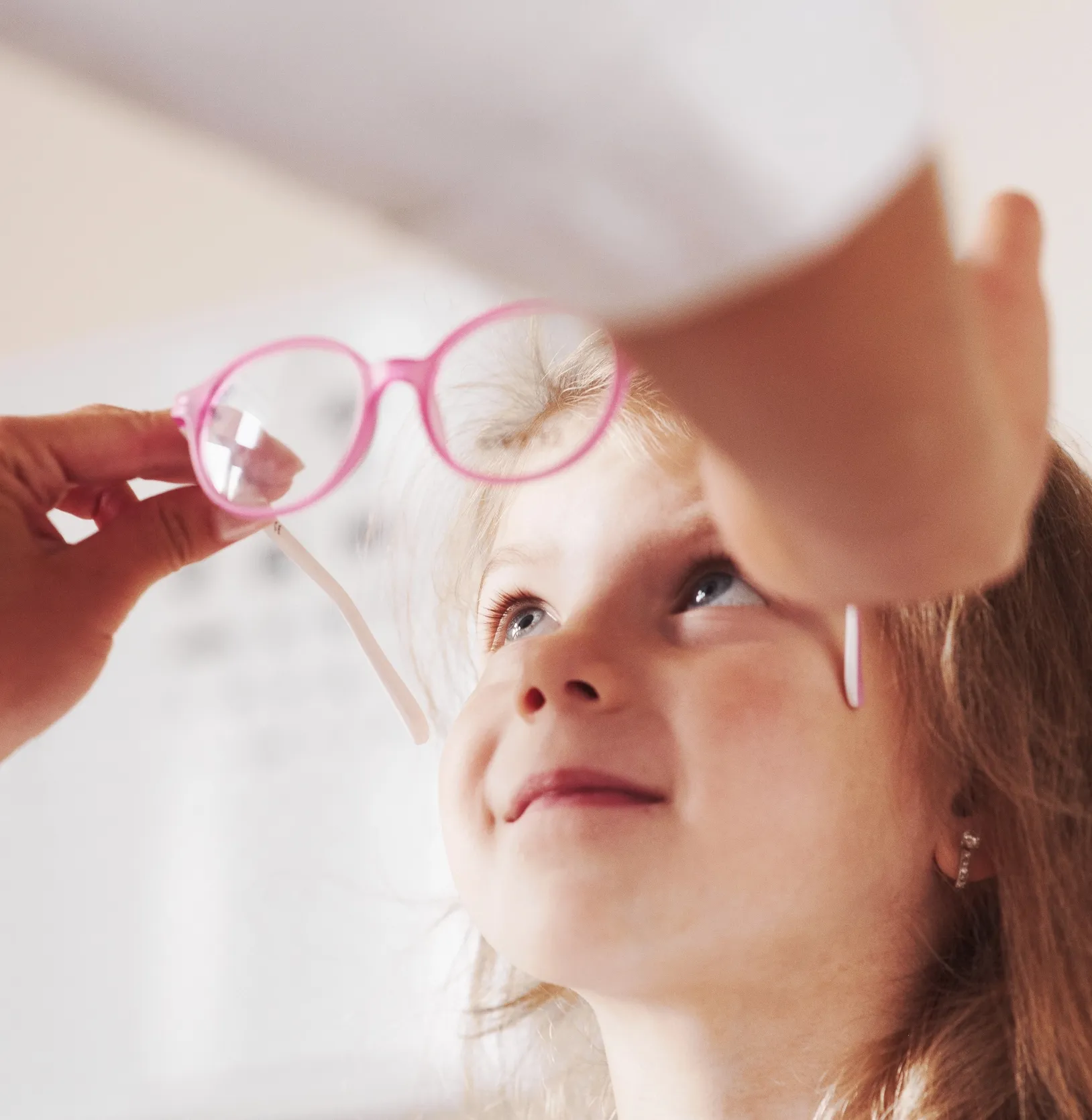 Ein Kind schaut erwartungsvoll auf eine Hand, die eine rosa Brille hält.